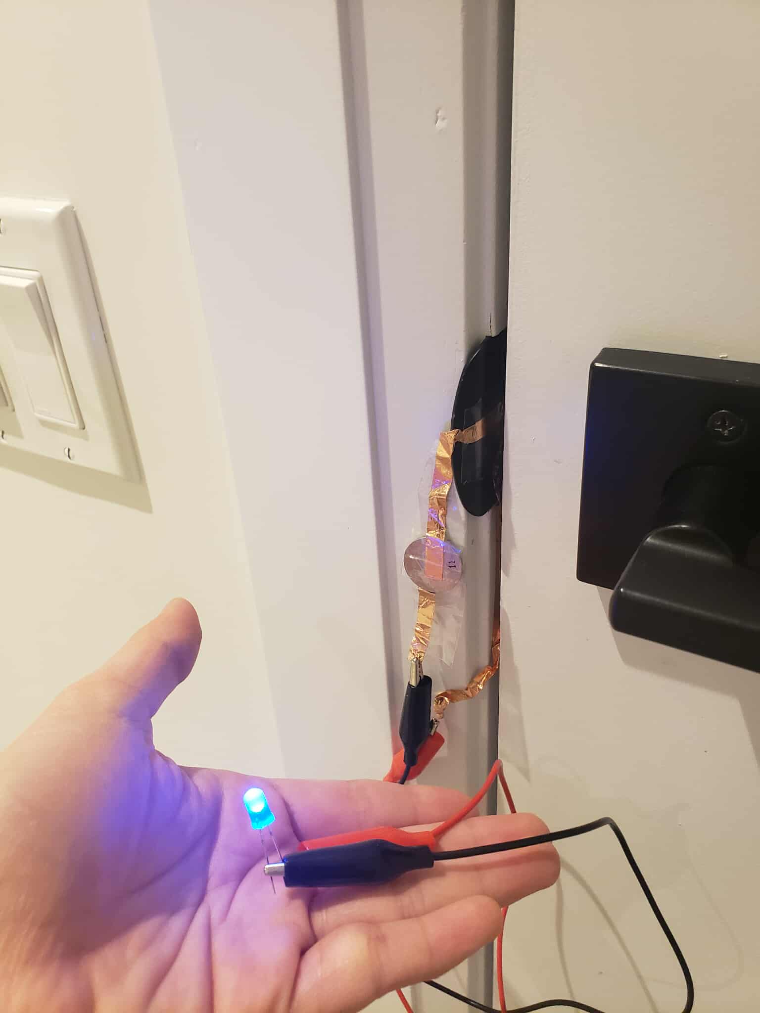 A turned on circuit using the conductive part of the other part of the door lock to complete the circuit. The extruded part of the door lock is conductive, and finishes the circuit when the door is closed.